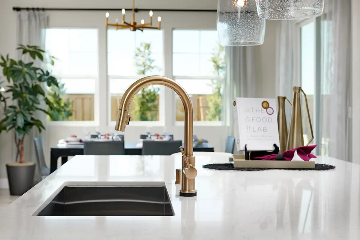 Island with quartz countertop, double sink, and gold faucet in front of dining area with three windows