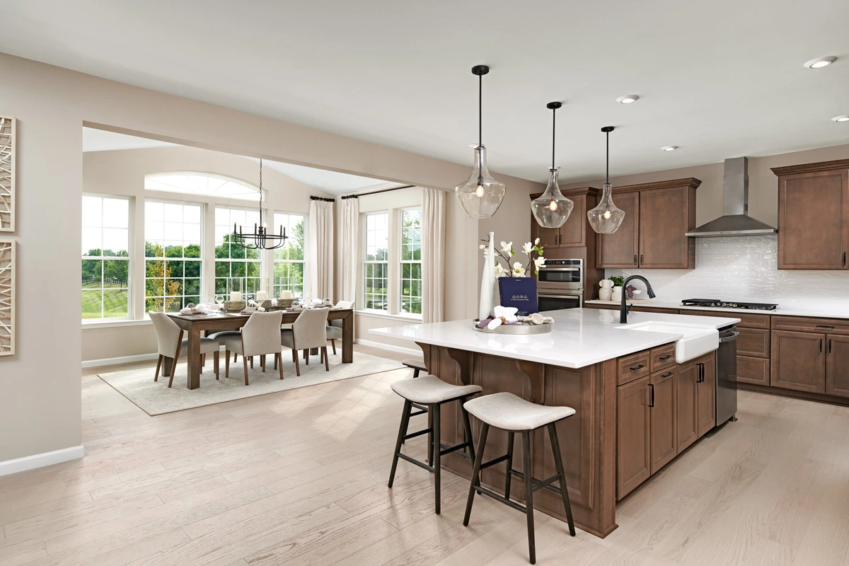 Kitchen with dark wood cabinets, a large island with farmhouse sink, next to a dining room surrounded by windows