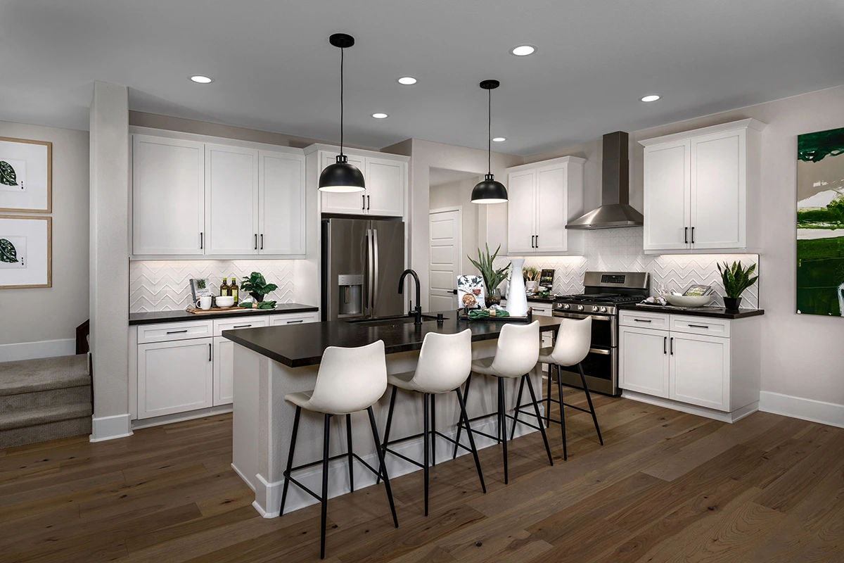 Kitchen with island with large sink, chevron textured backsplash, and dark wood floor, with stairs to the left of the kitchen