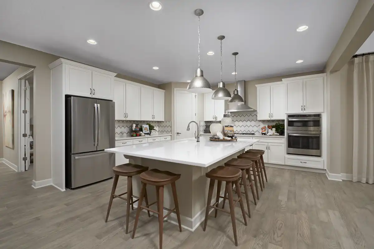 Kitchen with large island, patterned backplash, three large light fixtures and recessed lighting