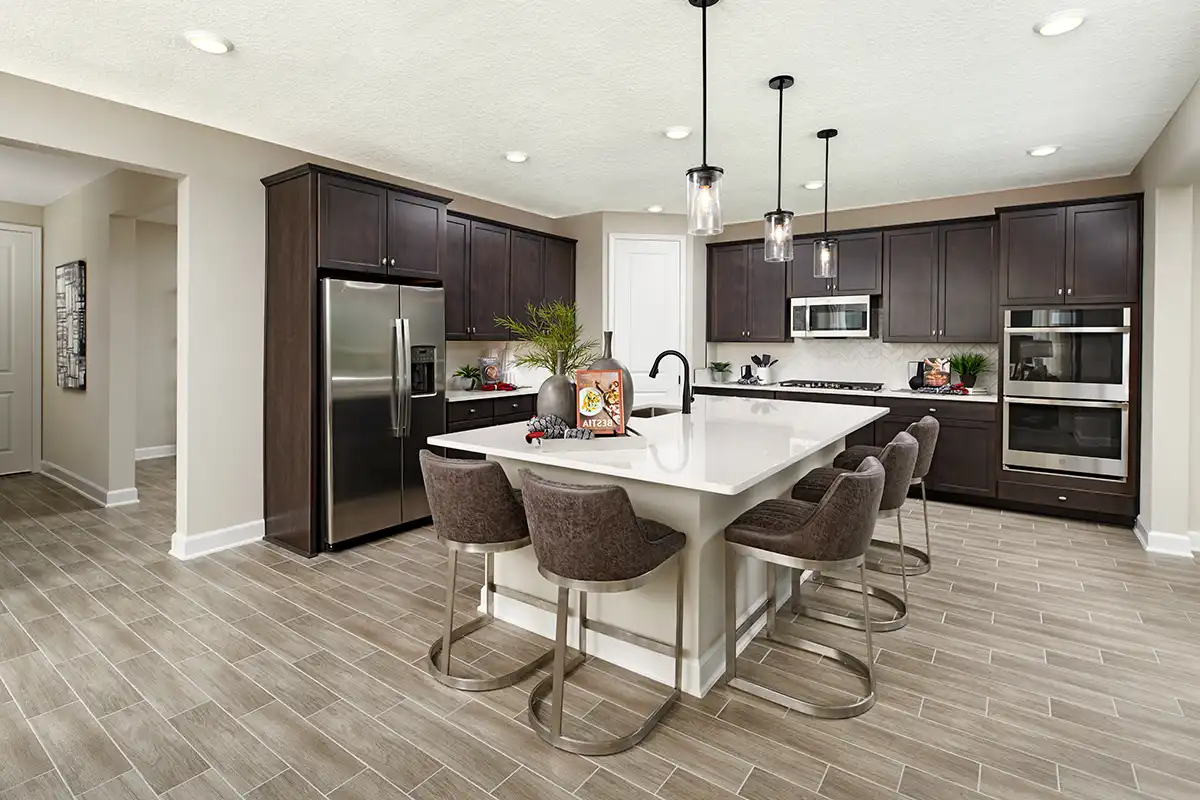 Kitchen with large island, dark cabinets, chevron tile backsplash, and double oven