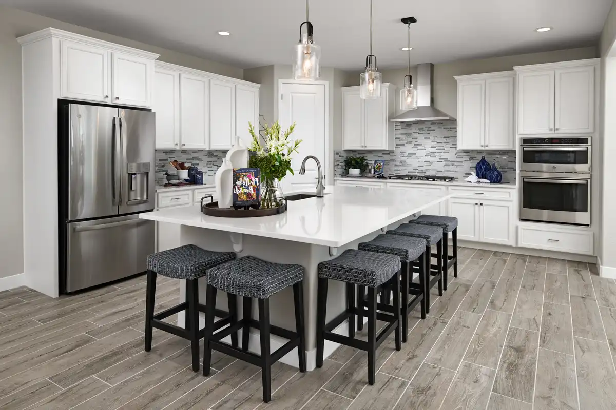 Kitchen with large island and three hanging lights above it, white backsplash, gas stove, and a double oven
