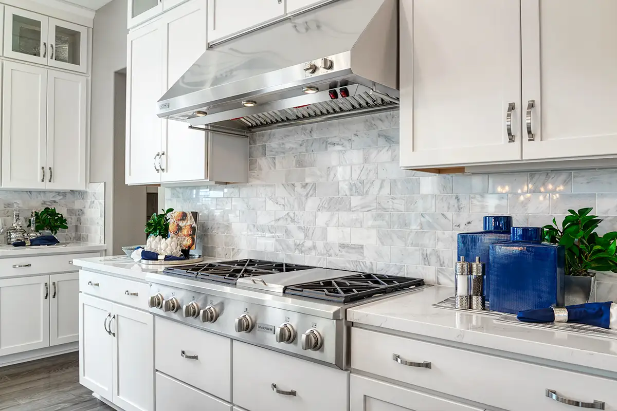 Large gas stove with brick-patterned backsplash and white cabinets