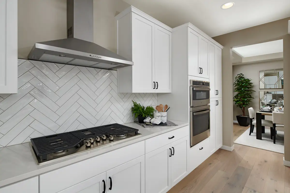 Wall of white kitchen cabinets with herringbone backsplash, a gas stove, double oven, and a doorway into a dining room