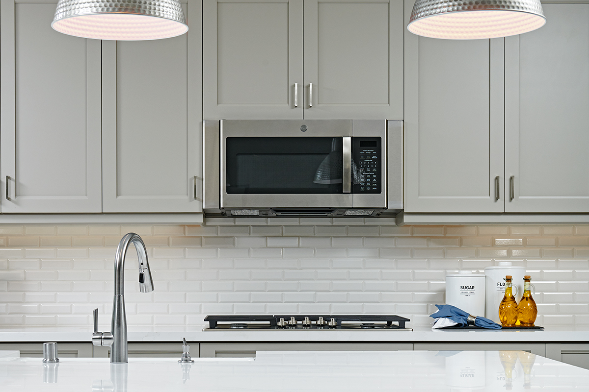 Upper cabinets with microwave above gas stove and brick-style backsplash