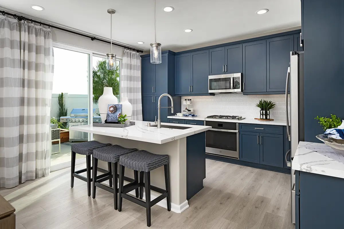 Kitchen with island, blue cabinets, white countertops and picket backsplash, with sliding doors to backyard with grill