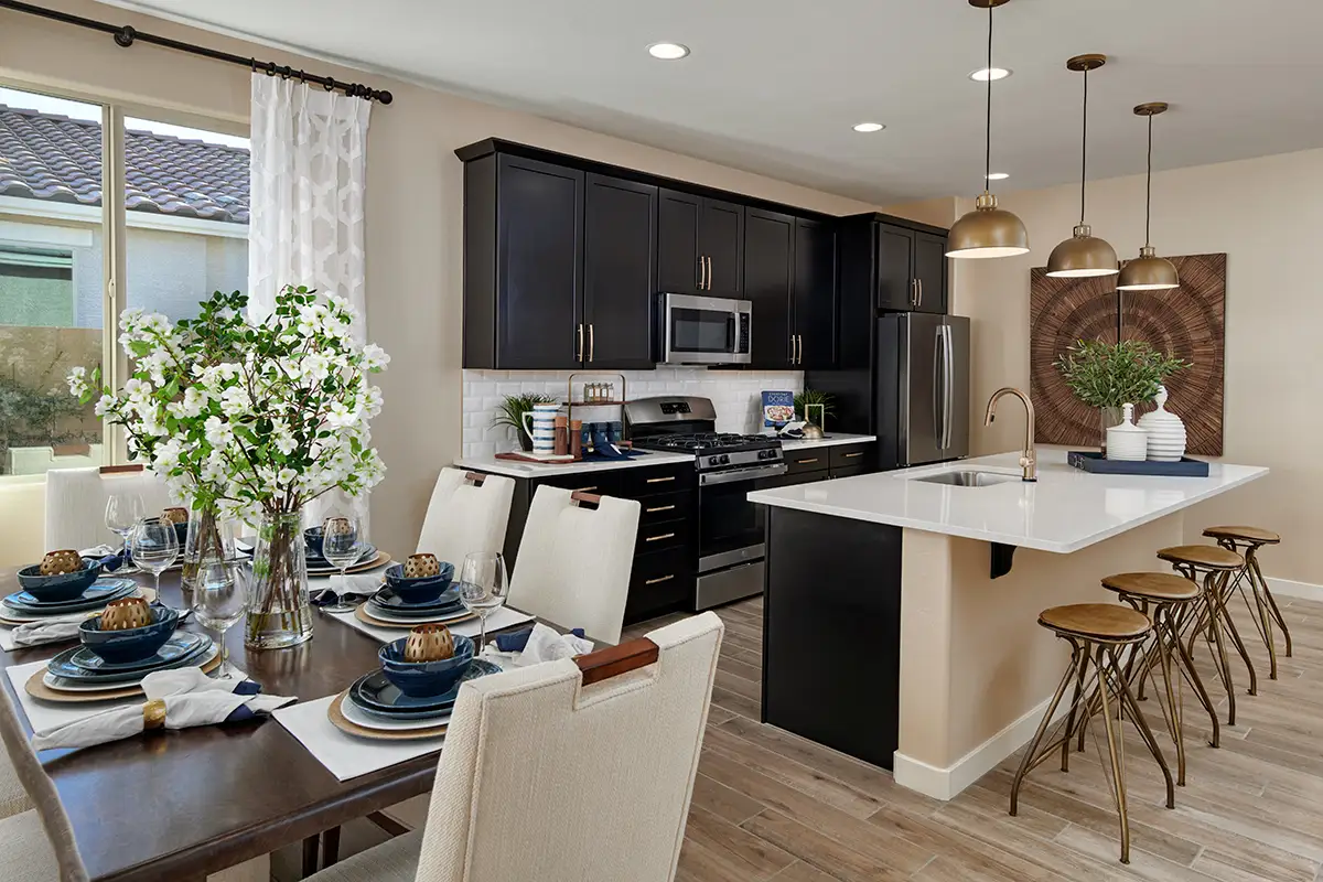 Dining table next to kitchen with black cabinets and gold hardware and island with four barstools