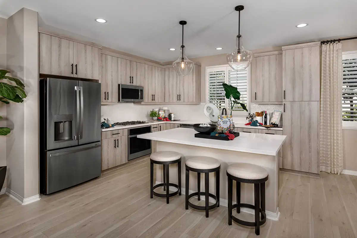 Kitchen with light wood cabinets and white countertops and an island with three barstools