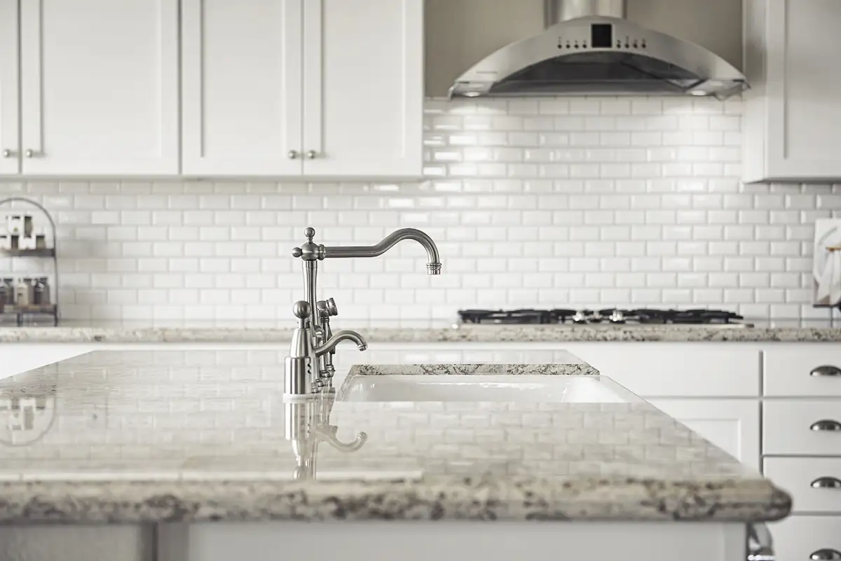 Island with granite countertop in front of cabinets with brick-style backsplash