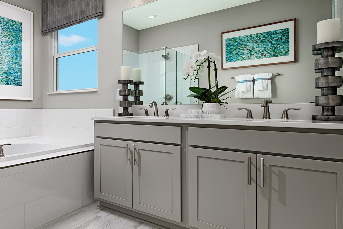 Two-sink vanity with gray cabinets, light countertops, and silver hardware below a large mirror and next to a tub