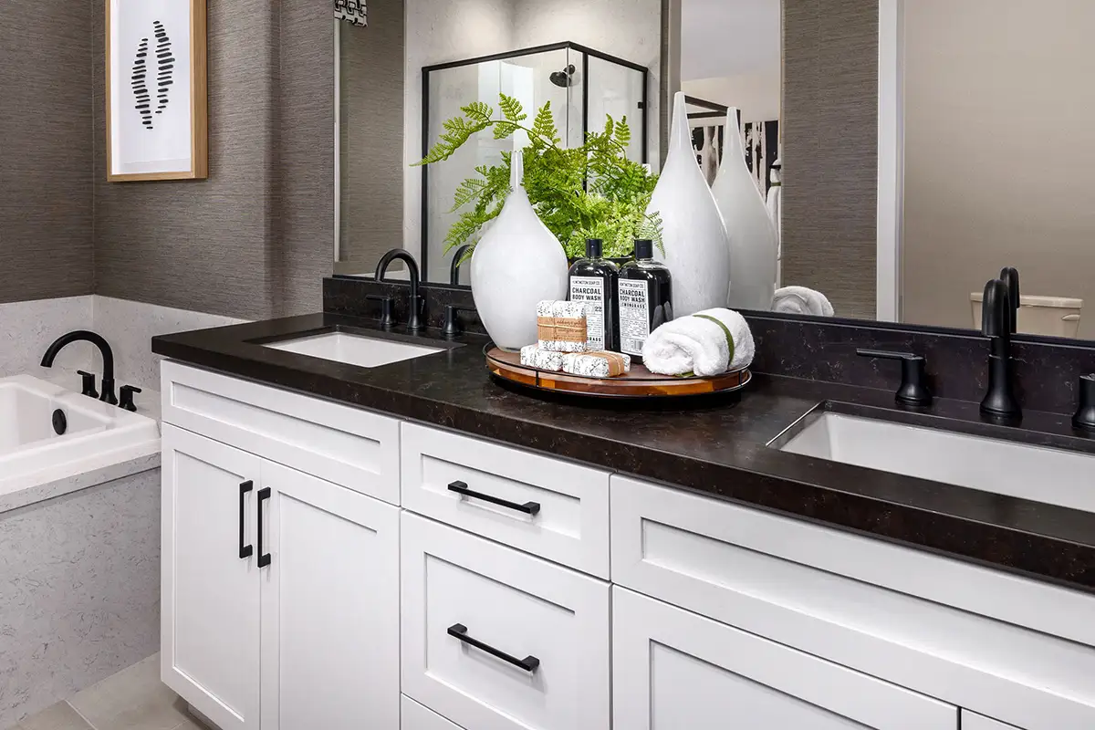 Two-sink vanity with white cabinets, dark countertops, and black hardware next to a white tub with black hardware
