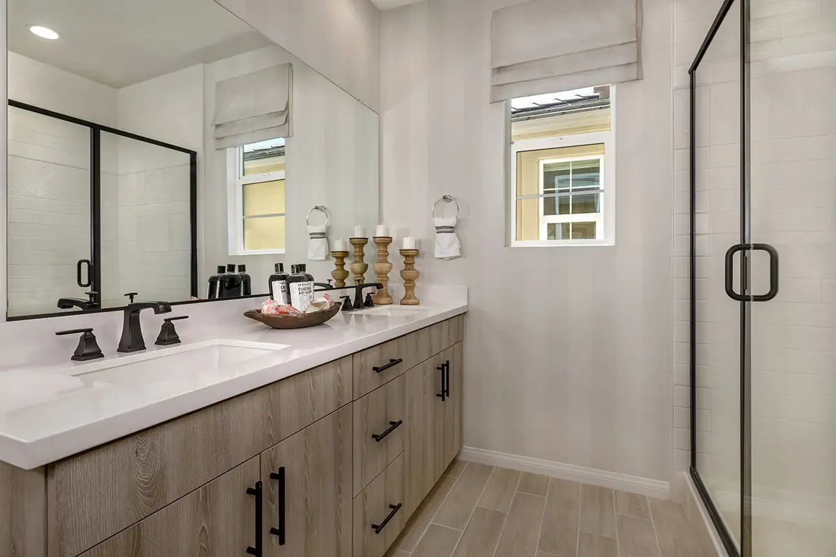 Two-sink vanity with light wood cabinets across from shower stall