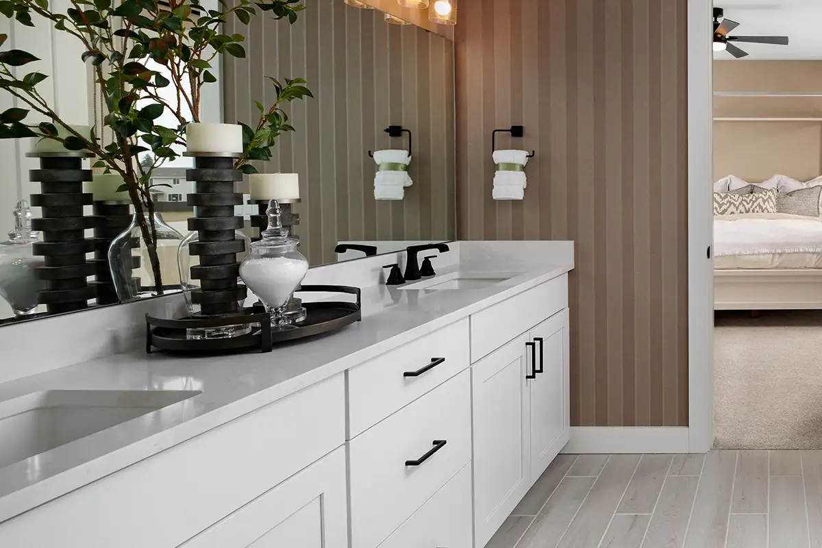 Large bathroom with double sinks, bathtub, striped wallpaper, and an open door leading into the owner's bedroom