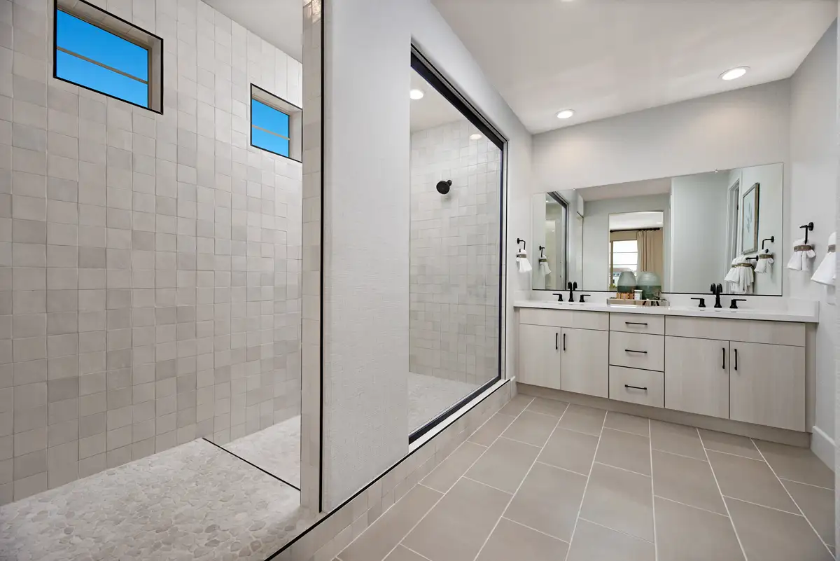 Bathroom with light double sink vanity with black hardware and step up to large shower stall with two small windows