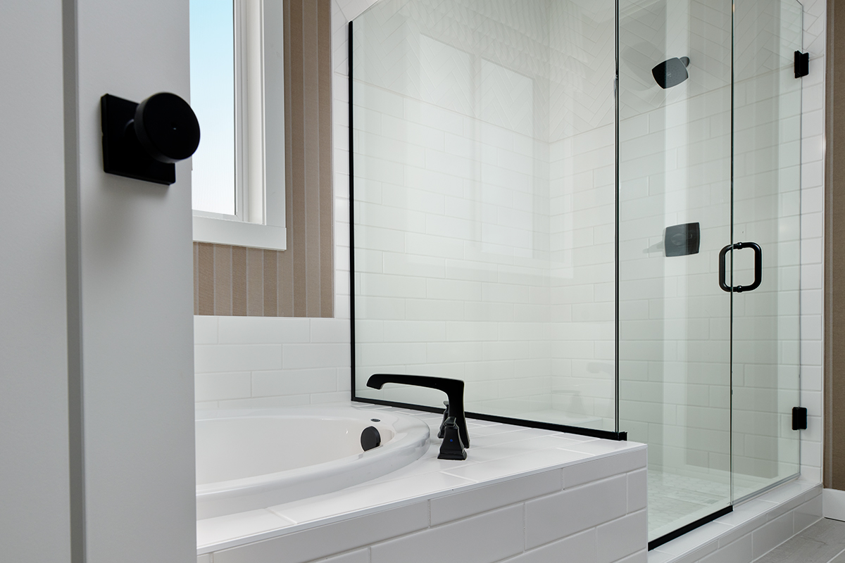 Bathroom tub next to window and shower stall with black hardware