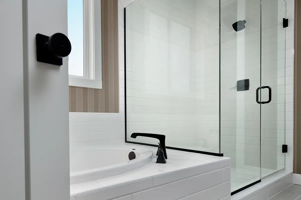 Bathroom tub next to window and shower stall with black hardware