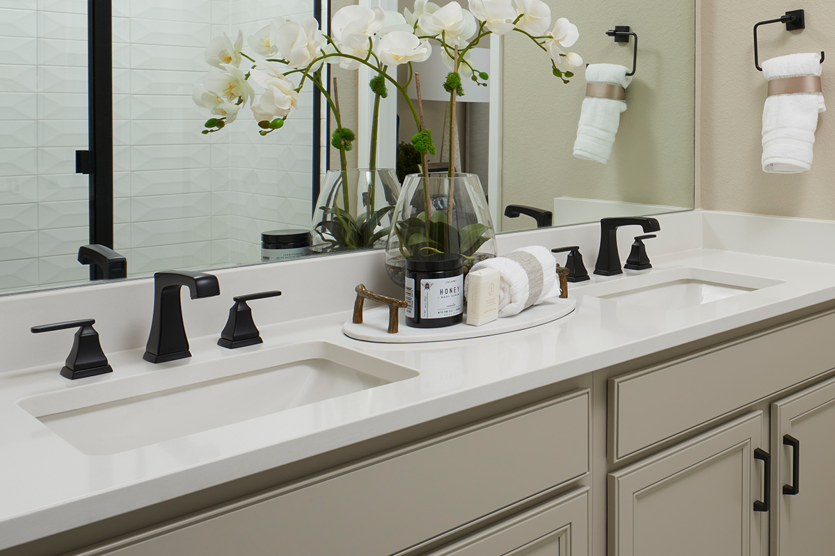Vanity with two sinks and modern black hardware below large mirror showing reflection of shower stall
