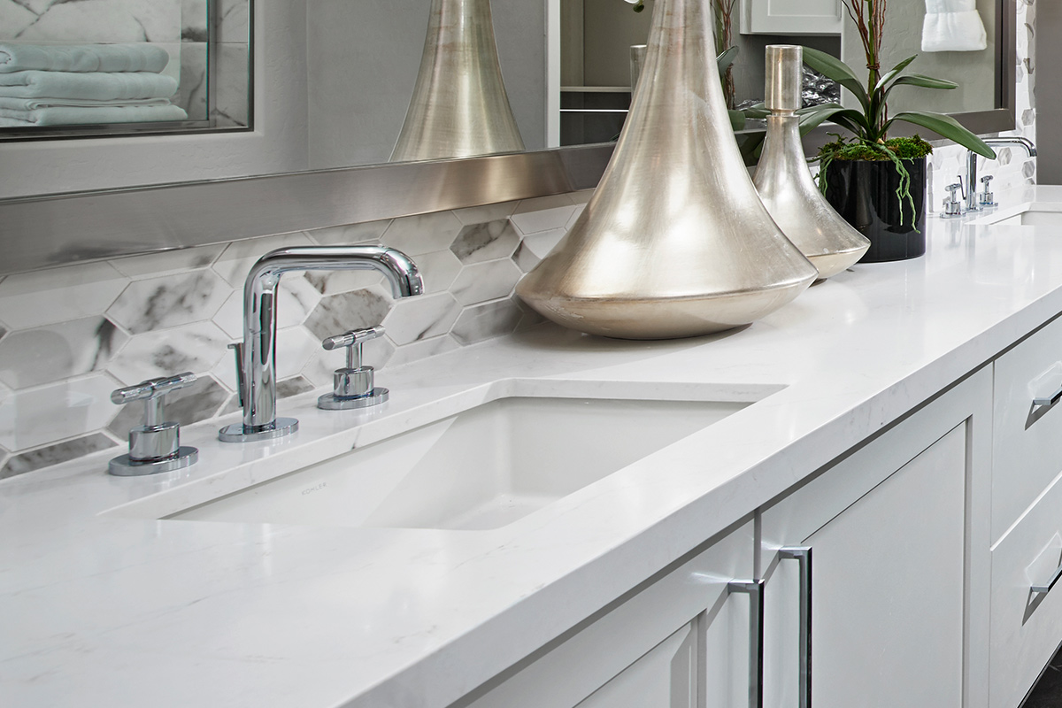 Bathroom vanity with white countertops and cabinets, silver hardware, and elongated hexagon tiles