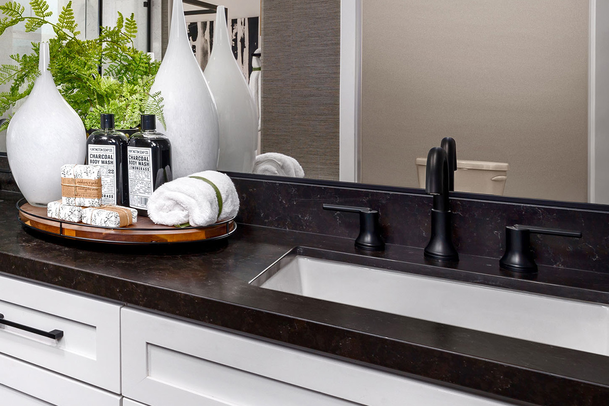 Bathroom vanity with black countertop, black hardware, and white cabinets below large mirror
